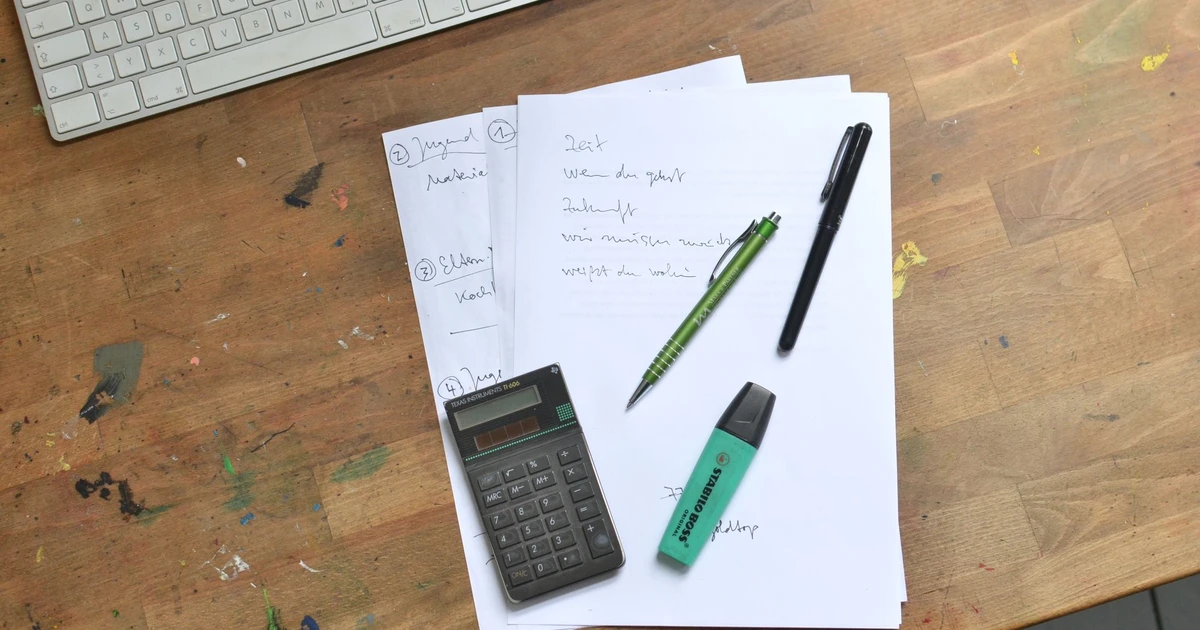 Tastatur, Taschenrechner und handschriftliche Kostenübersicht auf einem Schreibtisch